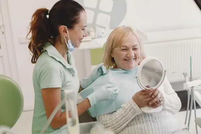 Dentist talking with a patient who holds a hand mirror